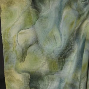 May include: Abstract textile with a watercolor effect. The fabric features a blend of green, blue, and yellow hues, creating a marbled or flowing pattern. The texture appears soft and slightly translucent, suggesting a lightweight material.