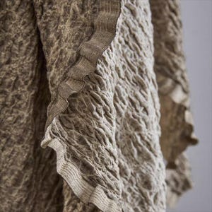May include: Close-up of a textured fabric in shades of brown and beige. The fabric has a crinkled appearance with a ruffled edge. The texture is detailed, creating a sense of depth and visual interest. The overall aesthetic is earthy and natural.