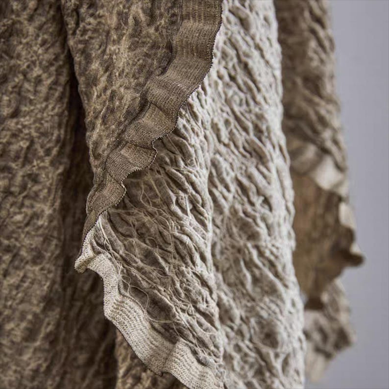 May include: Close-up of a textured fabric in shades of brown and beige. The fabric has a crinkled appearance with a ruffled edge. The texture is detailed, creating a sense of depth and visual interest. The overall aesthetic is earthy and natural.