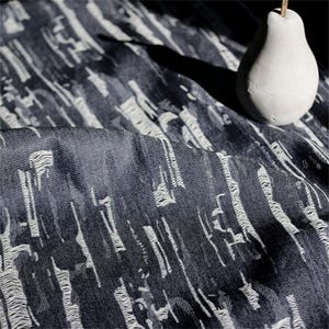 Peut inclure: Gros plan sur un tissu bleu foncé avec un motif abstrait blanc. Le tissu est drapé, montrant la texture et les plis. Un objet décoratif blanc en forme de poire avec une tige en bois est posé sur le tissu.