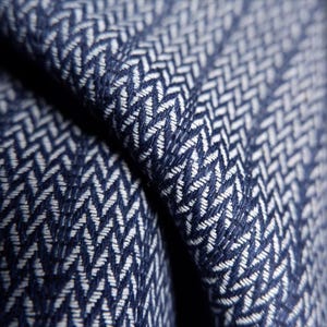 May include: Close-up of a folded fabric with a navy blue and white herringbone pattern. The fabric's texture is visible, with the weave creating a textured surface. The pattern is a classic design, suitable for various textile applications.
