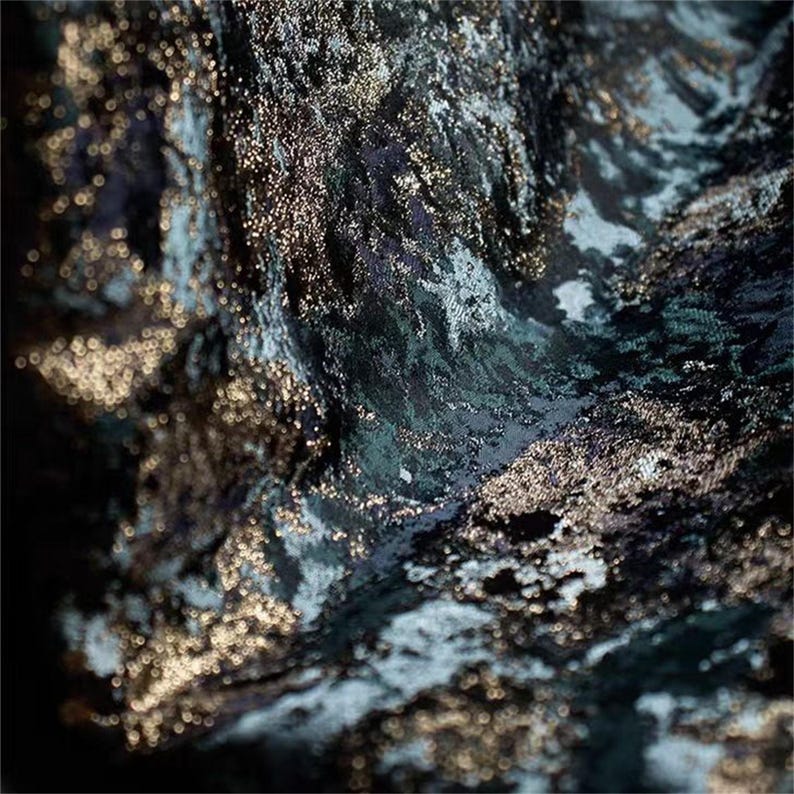 May include: Abstract image of a textured fabric with a dark teal and black base, accented with shimmering gold flecks. The fabric appears to be draped, creating a sense of depth and movement. The overall effect is luxurious and artistic.