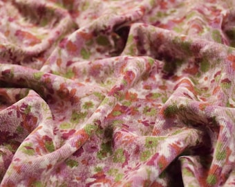 May include: Close-up of a floral fabric with a soft, textured appearance. The fabric features a pattern of small flowers in shades of pink, green, and orange against a light pink background. The fabric is gathered, creating soft folds and shadows.