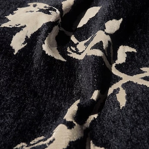 May include: Close-up of a dark blue fabric with a floral pattern in a lighter, off-white color. The fabric has a soft, textured appearance, with the floral design appearing to be slightly raised. The pattern is stylized and organic, with a flowing, artistic quality.