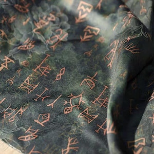 May include: Dark green fabric with a pattern of faded orange symbols and floral designs. The fabric has a textured appearance, with a slightly blurred effect, creating a vintage or antique aesthetic. The symbols are scattered across the surface.