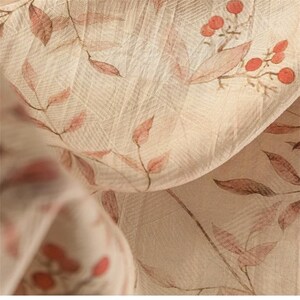 Op de afbeelding: Close-up van een beige stof met een delicaat bloemenpatroon. Het ontwerp toont takken met rode bessen en bladeren in roze en bruine tinten. De stof heeft een subtiele, getextureerde weefsel.