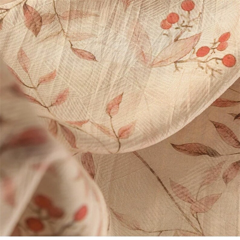 Op de afbeelding: Close-up van een beige stof met een delicaat bloemenpatroon. Het ontwerp toont takken met rode bessen en bladeren in roze en bruine tinten. De stof heeft een subtiele, getextureerde weefsel.