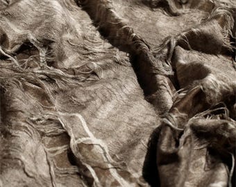 May include: Close-up of a textured, brown fabric with a distressed appearance. The fabric has a woven texture with visible strands and a slightly frayed edge. The color is a muted brown with highlights and shadows.