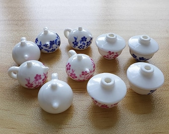 Puede incluir: Una colección de pequeñas teteras y cuencos de cerámica blanca. Algunos están decorados con diseños florales azules o rosas. Las teteras tienen asas y picos pequeños. Los cuencos tienen tapas. Los artículos están dispuestos sobre una superficie marrón claro.