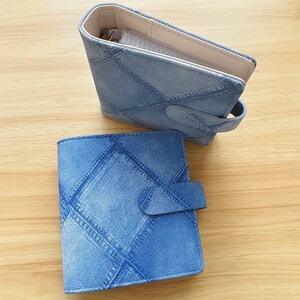 Puede incluir: Dos carteras de mezclilla. Una está abierta, revelando un interior beige y una cremallera. La otra está cerrada, con una solapa asegurada por un broche de presión. Ambas carteras tienen un patrón de diamantes y una apariencia de mezclilla azul claro.