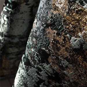 May include: Close-up of a textured fabric with a blend of colors. The fabric features a dark base with accents of gold, silver, and green, creating a shimmering effect. The design has a marbled or abstract pattern, suitable for upholstery or drapery.