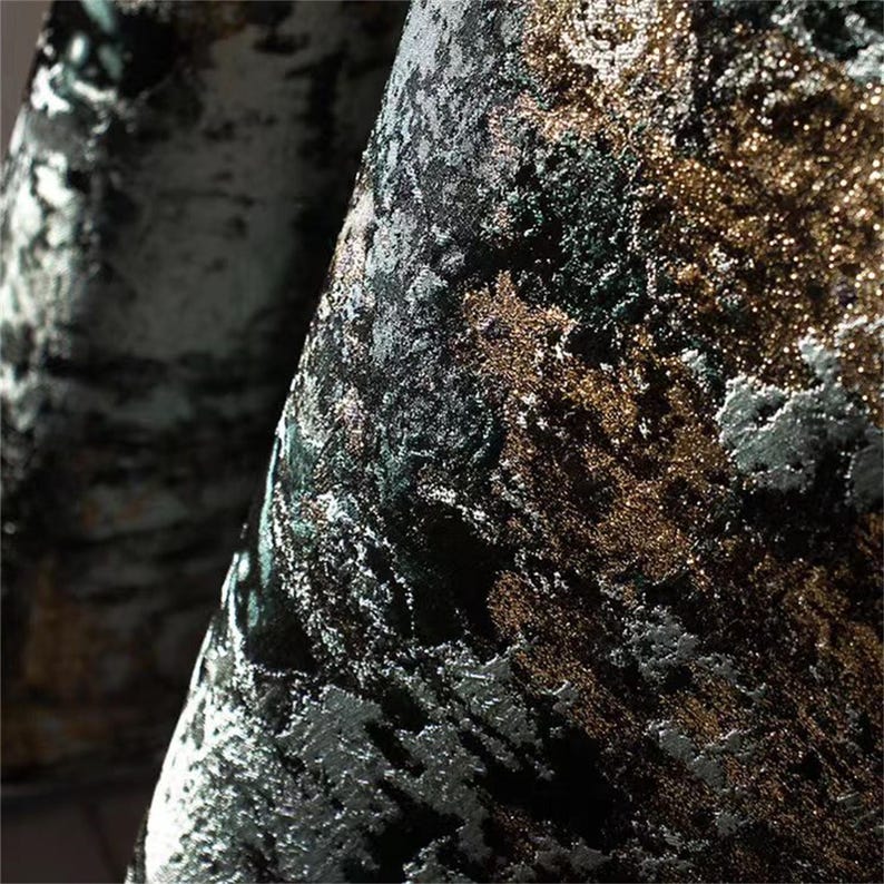 May include: Close-up of a textured fabric with a blend of colors. The fabric features a dark base with accents of gold, silver, and green, creating a shimmering effect. The design has a marbled or abstract pattern, suitable for upholstery or drapery.