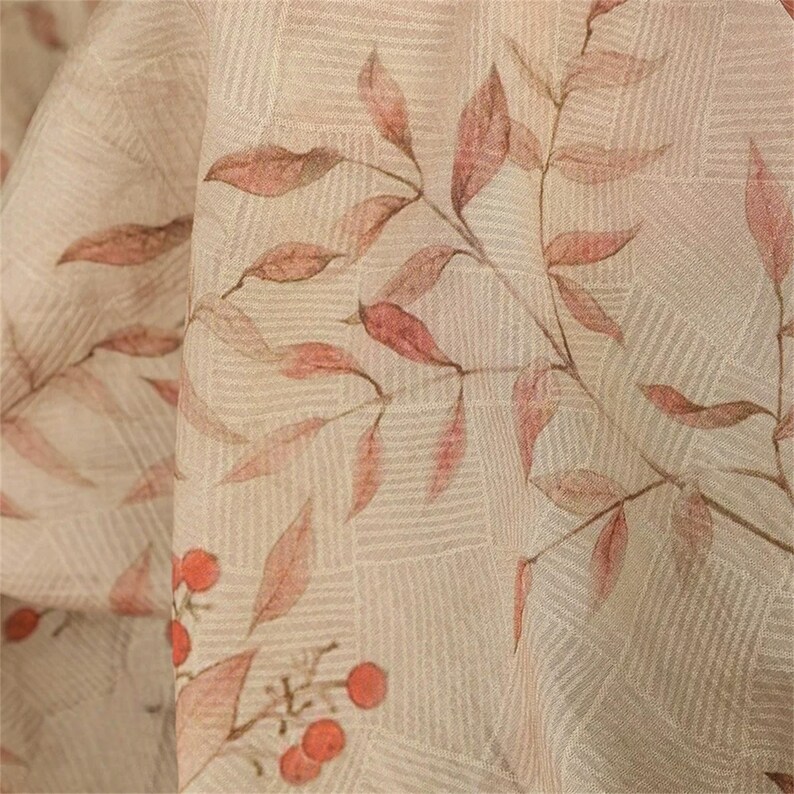 Op de afbeelding: Close-up van een beige stof met een subtiel rasterpatroon. Sierlijke takken met roodbruine bladeren en kleine oranje bessen zijn kunstzinnig op het oppervlak gedrukt, wat een natuurlijk, botanisch ontwerp cre&euml;ert.