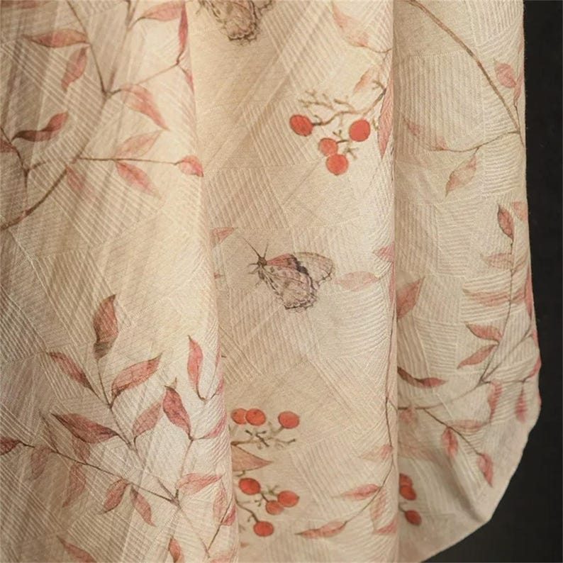 Op de afbeelding: Close-up van een stof met een cr&egrave;mekleurige achtergrond. De stof heeft een herhalend patroon van bladeren, bessen en vlinders in roze en bruine tinten. De stof heeft een getextureerd uiterlijk.