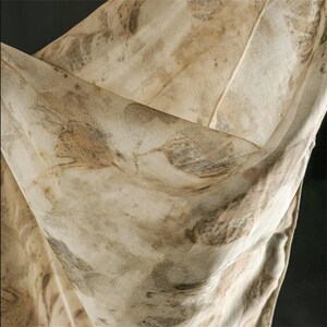 May include: A lightweight, semi-sheer fabric scarf featuring an organic botanical print in shades of beige, cream, and muted brown. The textile displays intricate, detailed leaf imprints scattered across the surface, creating a natural, earthy pattern with soft folds and draped textures throughout the material.