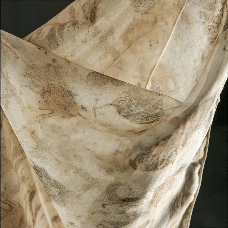 May include: A lightweight, semi-sheer fabric scarf featuring an organic botanical print in shades of beige, cream, and muted brown. The textile displays intricate, detailed leaf imprints scattered across the surface, creating a natural, earthy pattern with soft folds and draped textures throughout the material.