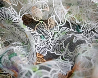 May include: Close-up of sheer fabric with a floral design. White, delicate floral outlines are layered over a dark background. Hints of green, orange, and purple add color to the design. The fabric is slightly wrinkled.