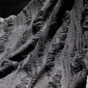 Puede incluir: Primer plano de una tela negra con un diseño desgastado y texturizado. La tela tiene una apariencia ondulada con detalles verticales deshilachados, creando un efecto visual único. El color oscuro y la textura sugieren un enfoque en la moda gótica o alternativa.