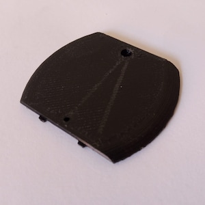 May include: A black, curved, 3D-printed object with a textured surface. It has a rounded shape with a flat edge and two small holes. The object appears to be a component or part of a larger item.