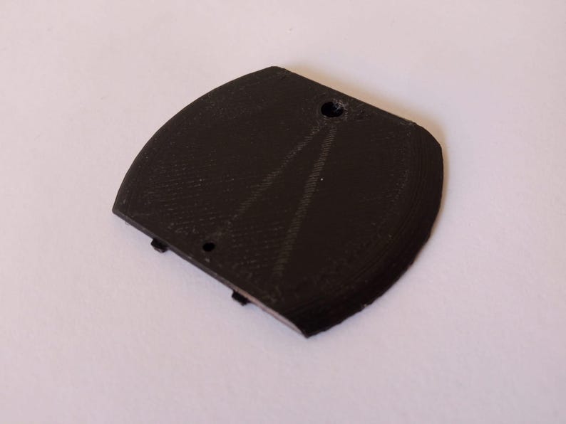 May include: A black, curved, 3D-printed object with a textured surface. It has a rounded shape with a flat edge and two small holes. The object appears to be a component or part of a larger item.