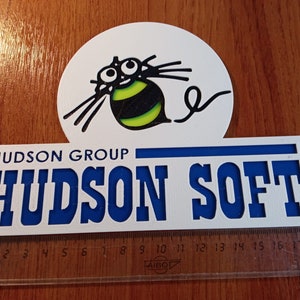 Puede incluir: Un cartel blanco con letras azules que dice "HUDSON GROUP" y "HUDSON SOFT". Una abeja de dibujos animados con rayas negras y amarillas y ojos grandes est&aacute; por encima del texto.