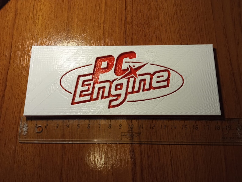 Puede incluir: Un letrero rectangular blanco con un logotipo 3D rojo que dice "PC Engine" con una estrella en la "C".