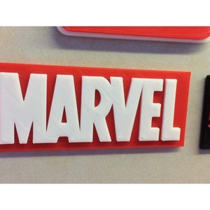 Puede incluir: Un letrero rectangular rojo con la palabra "MARVEL" en letras blancas.