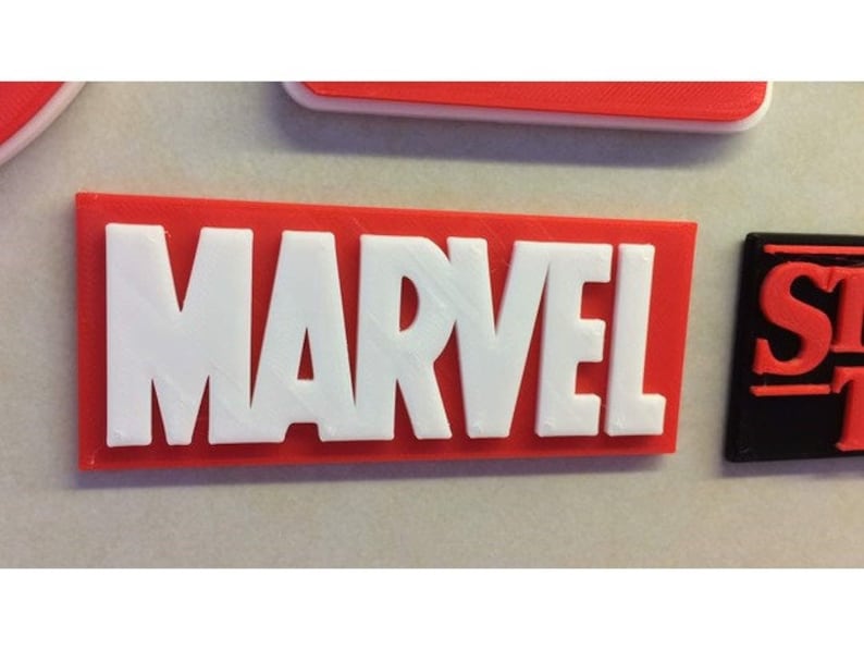 Puede incluir: Un letrero rectangular rojo con la palabra "MARVEL" en letras blancas.