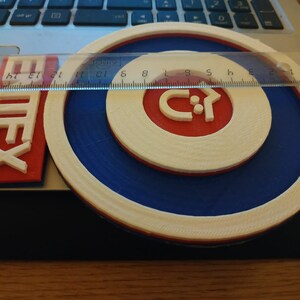 Puede incluir: Un logotipo impreso en 3D blanco, azul y rojo con el texto "Emtex" y una flecha estilizada que apunta hacia la derecha. El logotipo est&aacute; sobre una superficie de madera.