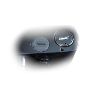 May include: Close-up of a black object with two circular openings. One opening has a rectangular slot, and the other has a keyhole design. The object appears to be made of a smooth, possibly metallic material.