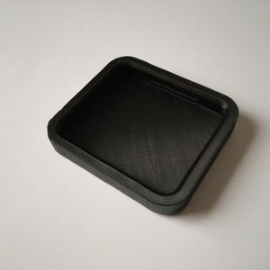 Peut inclure: Un récipient carré en plastique noir avec un bord surélevé.