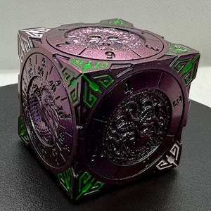 May include: A metallic purple cube with intricate designs and green accents. The cube features circular clock-like faces with embossed figures and numbers. The edges have geometric patterns, and the overall aesthetic is detailed and ornate.