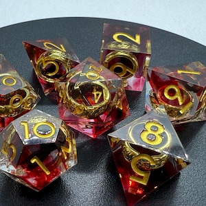 May include: Set of seven red and gold dice with a swirl pattern and gold rings. The dice are made of clear resin and have a variety of numbers on each side.