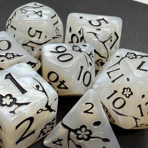 May include: Set of seven pearlescent white dice with black numbers and floral designs. Includes a variety of shapes, such as a d4, d6, d8, d10, d12, d20, and a percentile die. Ideal for tabletop games.