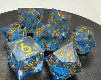 May include: A set of seven blue and gold dice with a glittery finish. The dice have a variety of numbers and symbols on them, including a koi fish design.