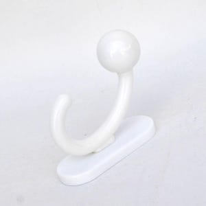 Peut inclure: Un crochet mural blanc incurvé avec un dessus arrondi et une base rectangulaire. Le crochet est conçu pour suspendre des objets et est fait d'un matériau lisse et brillant. Le crochet mesure environ 10 cm de haut.