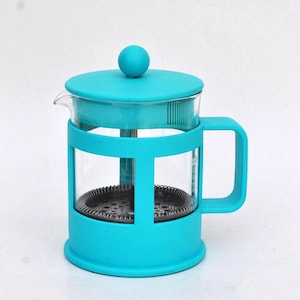 Può includere: Una caffettiera a pistone turchese con una caraffa in vetro e un coperchio e manico abbinati. La pressa ha una forma cilindrica con un filtro a rete metallica all'interno. Il manico è sul lato destro e il coperchio ha una piccola sfera sopra.