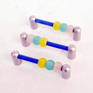 May include: Three cabinet pulls with a blue central bar, silver ends, and colourful beads. The beads are yellow, light blue, and frosted pink. These decorative pulls are for furniture and home decor.