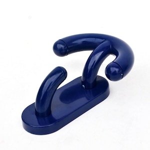 Pode incluir: Um gancho de parede de plástico azul escuro com um design curvo. O gancho tem uma base retangular com dois braços curvos que se estendem para cima e um terceiro braço curvo que se estende da base. O gancho foi projetado para pendurar itens.