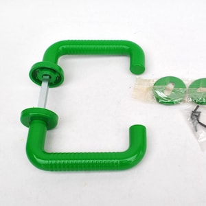 Op de afbeelding: Twee heldergroene deurgrepen met een geribbeld ontwerp, samen met twee groene ringen en een kleine inbussleutel. De handgrepen zijn L-vormig, de hardware op een witte achtergrond.