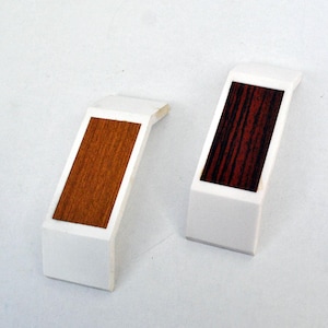 Puede incluir: Dos piezas de esquina de plástico blanco con insertos de veta de madera. Una pieza tiene un inserto de veta de madera marrón y la otra tiene un inserto de veta de madera rojo oscuro. Se incluyen tres tornillos plateados.