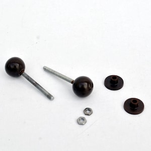 Könnte beinhalten: Zwei braune Holzgriffe mit Metallschrauben und zwei passenden Metallunterlegscheiben. Zwei silberne Muttern sind ebenfalls enthalten.