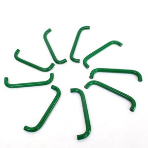 May include: A collection of eleven green metal hooks arranged in a circular pattern against a white background. Each hook has a curved shape with a straight middle section and bent ends. The hooks are evenly spaced.