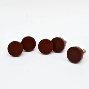 Op de afbeelding: Zes ronde, donkerbruine houten meubelknoppen met zilverkleurige hardware worden gepresenteerd tegen een witte achtergrond. De knoppen zijn gelijkmatig verdeeld, wat hun eenvoudige, minimalistische ontwerp benadrukt. Geschikt voor meubel- en woondecoratieprojecten.