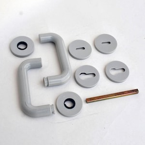 Puede incluir: Un juego de manillas de puerta grises con una varilla de metal plateado. El juego incluye dos manillas, cuatro placas redondas y una varilla.
