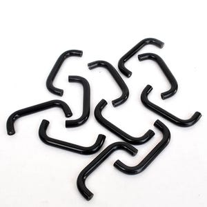 Puede incluir: Un conjunto de piezas metálicas negras y curvadas, cada una con forma redondeada. Las piezas están dispersas sobre una superficie blanca, creando una disposición visualmente interesante. Parecen ser componentes de ferretería.