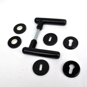 May include: Black door handles and keyhole covers. The door handles have a T-shape design with a silver connecting rod. The keyhole covers are round with a keyhole cutout and a white ring around the centre.