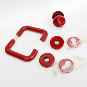 May include: A collection of red door hardware, comprising a handle, a knob, and several round escutcheons. The items are new and unused, with some still in their original packaging. The components are metal with a glossy finish. The hardware is for a door.