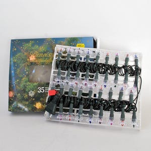 Op de afbeelding: Een set van 35 doorzichtige miniatuurlampjes aan een donkergroen snoer, gerangschikt in een witte plastic tray. De verlichting is verpakt in een rechthoekige kartonnen doos met een afbeelding van een versierde kerstboom.