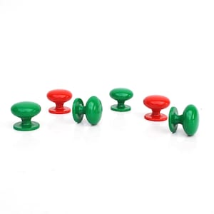 May include: A collection of six colorful cabinet knobs in red and green. The knobs have a rounded, oval shape and are arranged on a white surface. The knobs are likely for furniture or decorative purposes.